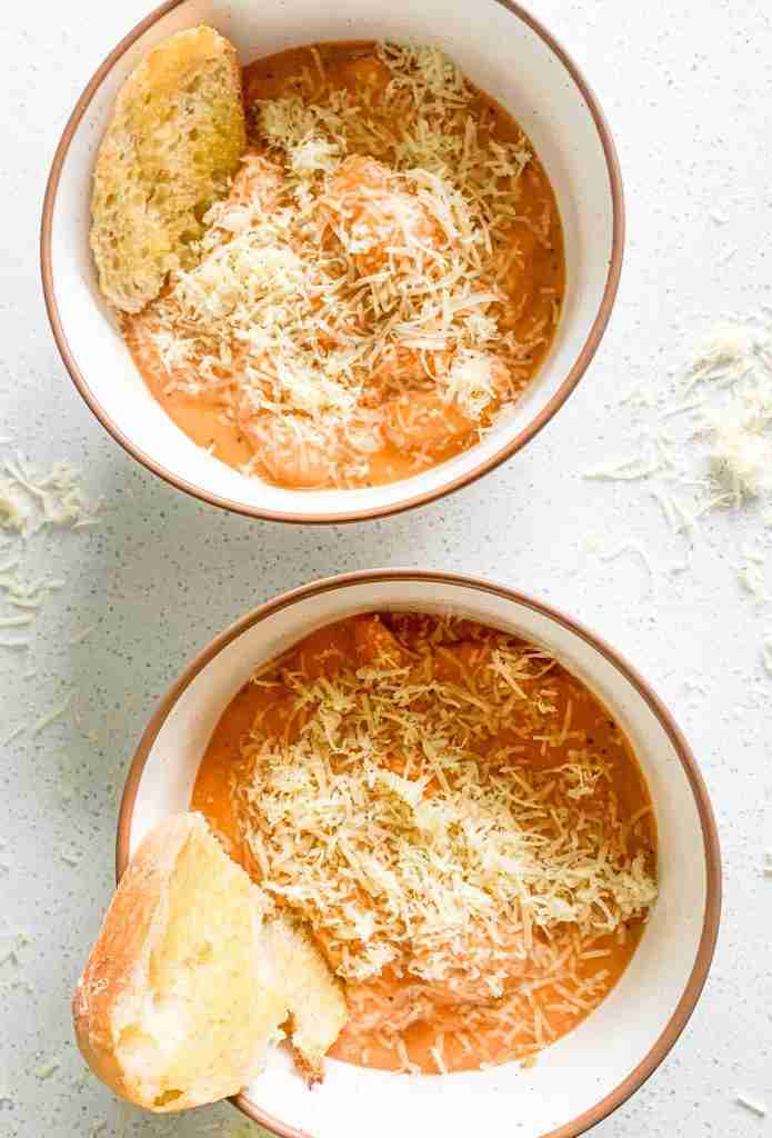 2 bowls of red soup with cheese on top and bread