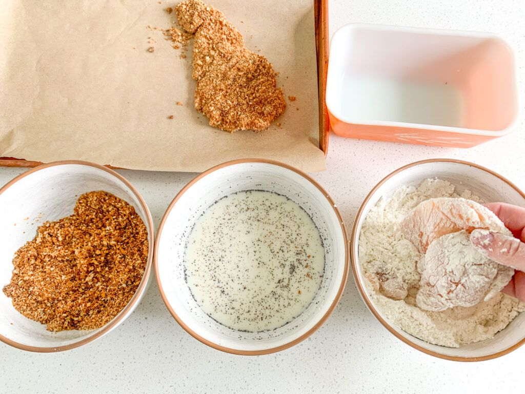 dredging chicken breast in breading for chicken sandwich