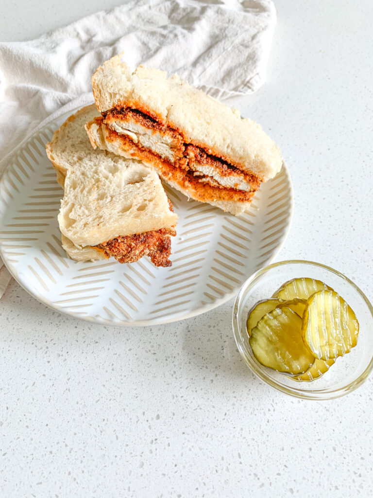Freshly made Nashville Hot Chicken sandwich cut in half with a side of pickles