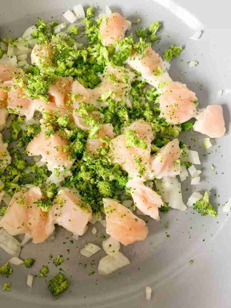 uncooked chicken in a skillet with onions and broccoli