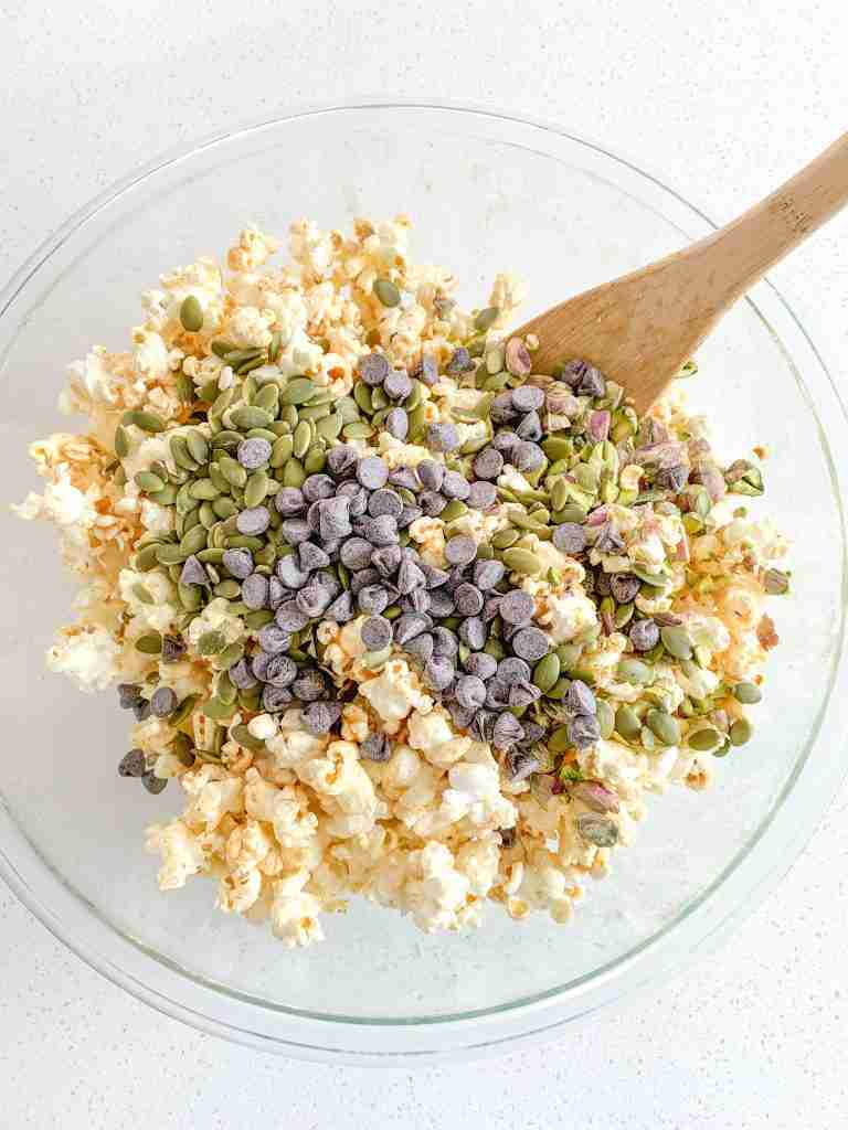 all ingredients in a bowl getting mixed together for snack mix