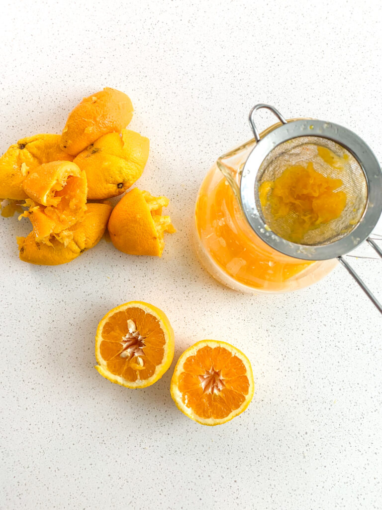 squeezing fresh orange juice into pitcher through a strainer