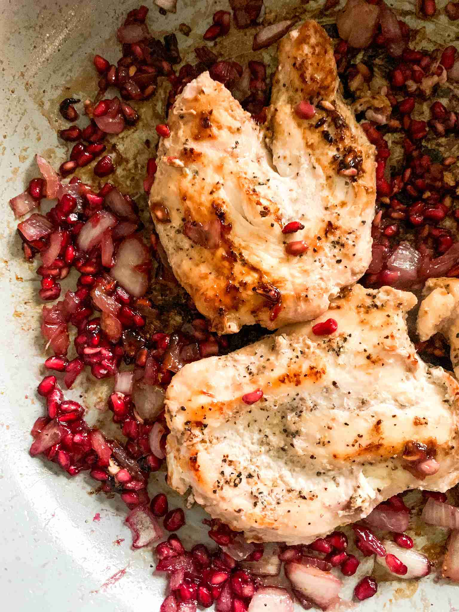 chicken breasts in skillet with pomegranates