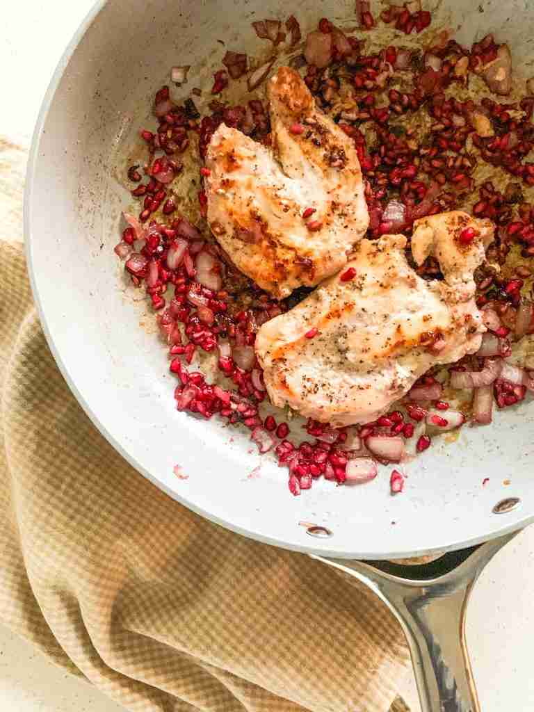 chicken breasts in a skillet with pomegranate seeds