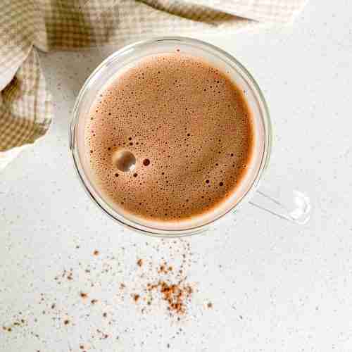 glass mug of hot chocolate with a towel laying beside it