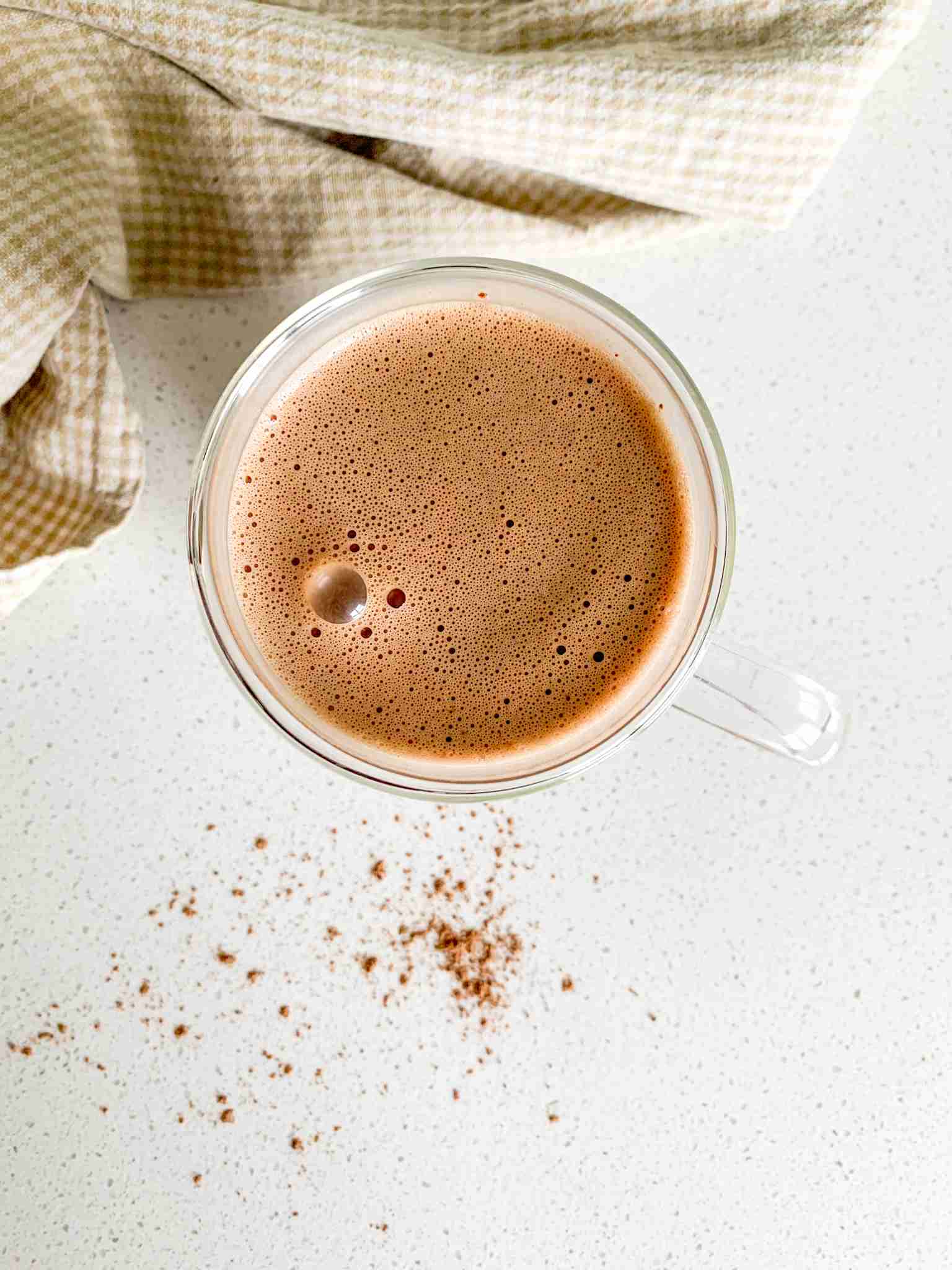 glass mug of hot chocolate with a towel laying beside it