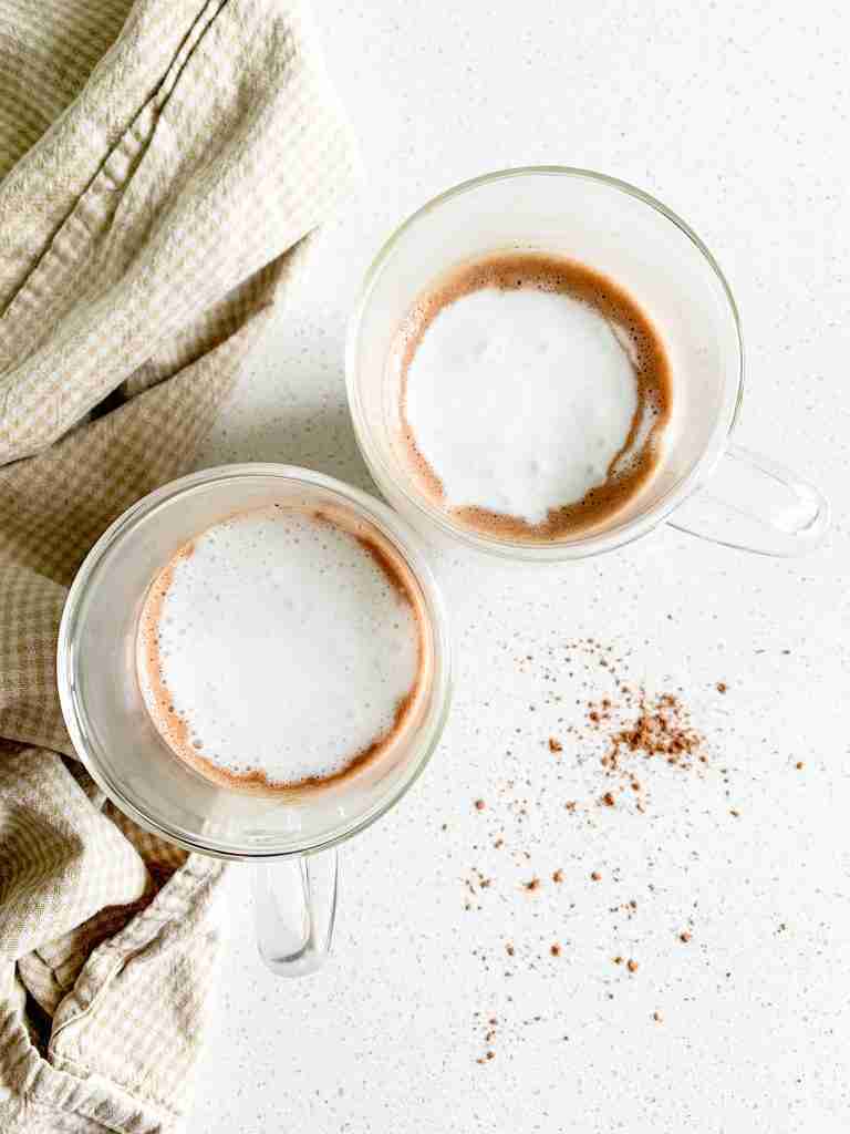 2 mugs of hot cocoa with whipped cream on top 