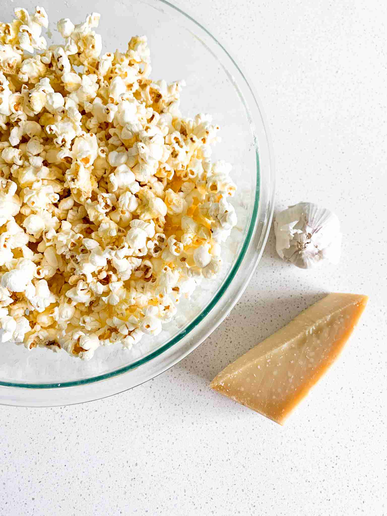 bowl of popcorn with a head of garlic beside it and a wedge of cheese