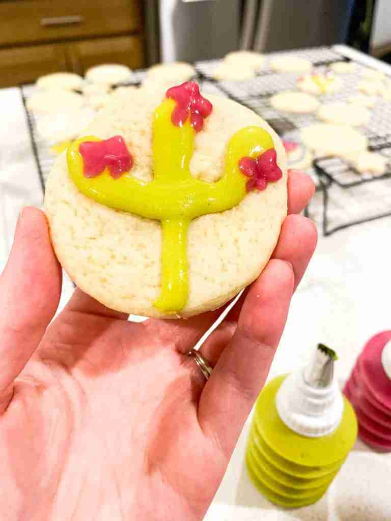 hand holding up a decorated cookie with a cactus design 