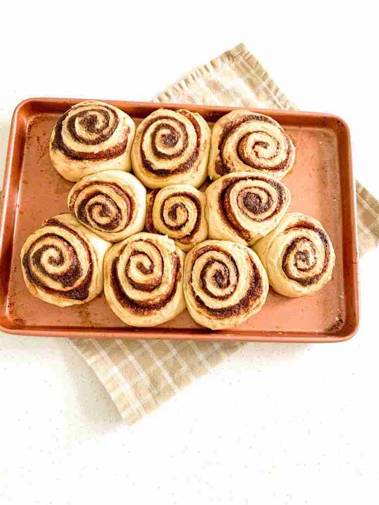 pink sheet pan full of baked cinnamon buns and a towel underneath