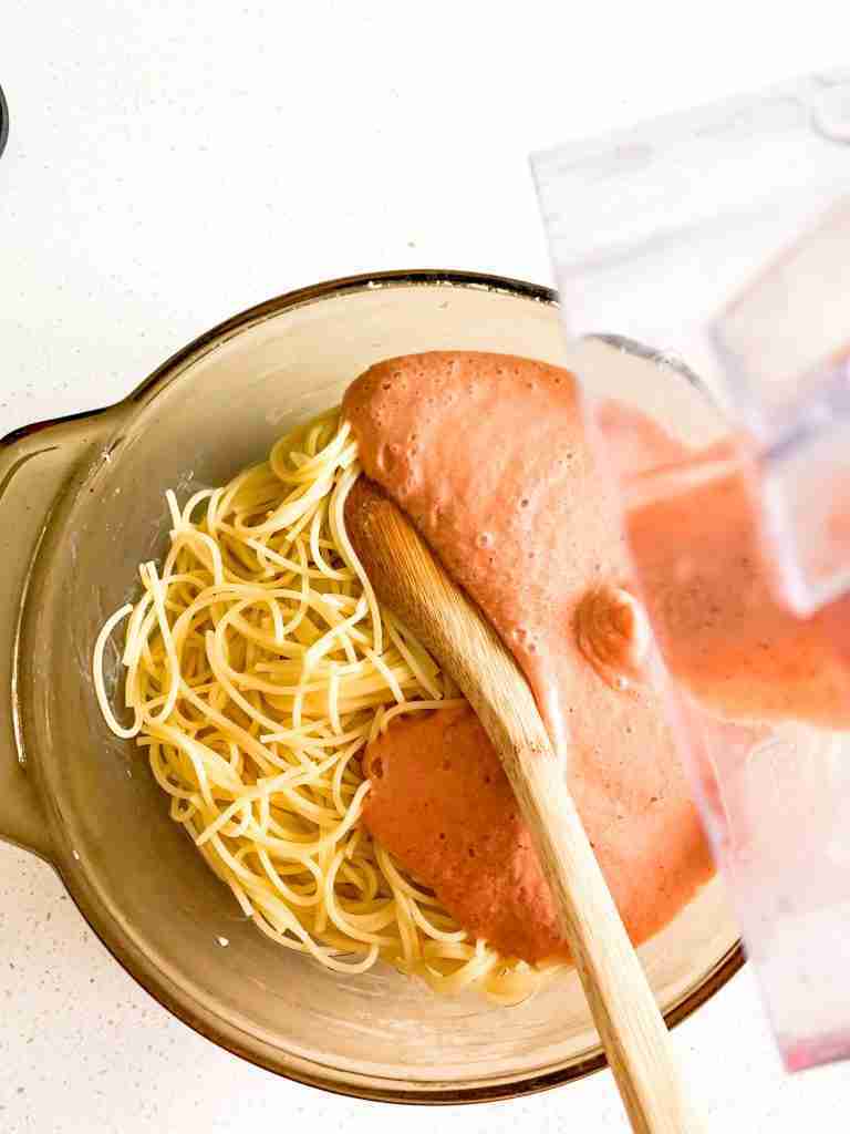 sauce being poured into a casserole dish full of spaghetti noodles