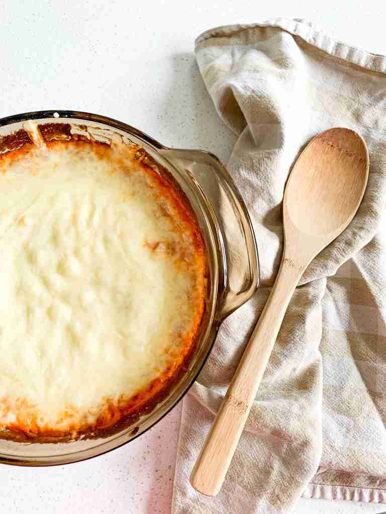 casserole dish full of cheesy pasta with a wooden spoon next to it on a towel ready to be served