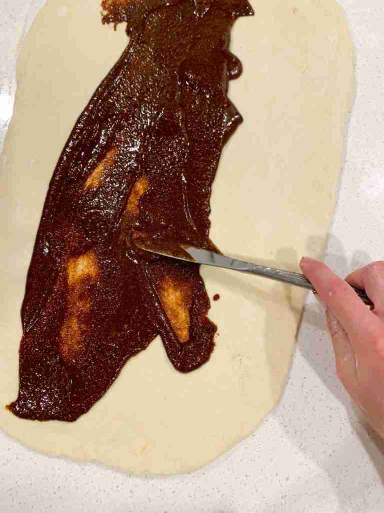 hand spreading cinnamon sugar on dough