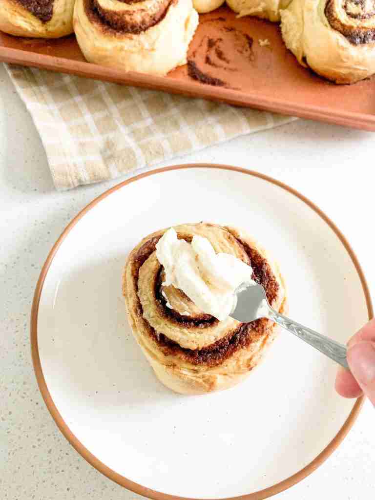 hand spreading frosting on cinnamon bun
