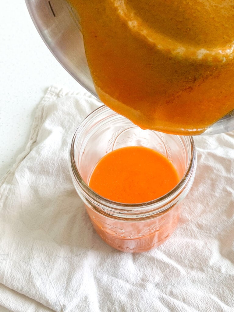homemade buffalo sauce getting poured in a storage jar