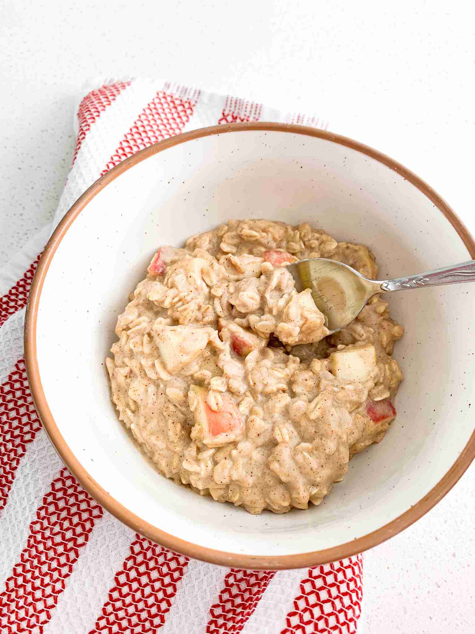 bowl of oatmeal with chunks of apple in it and a spoon with the bowl resting on a towel