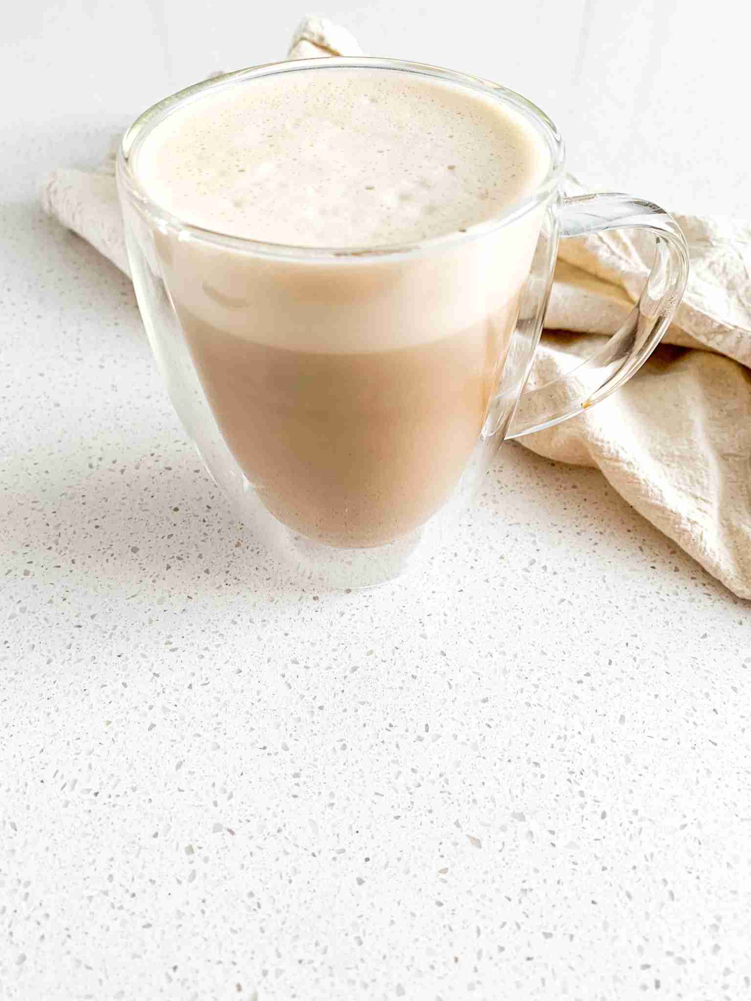 mug of coffee with foam on top of it with a towel behind it