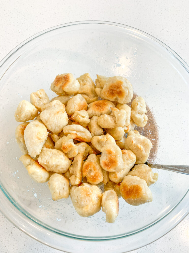 freshly baked sourdough pretzel bites being tossed in melted butter in a bowl