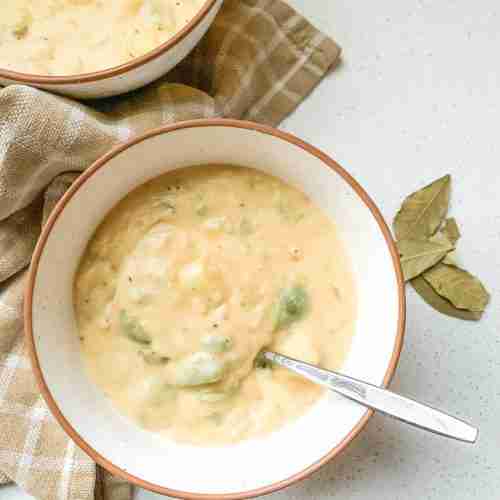 bowls of soup with veggies inside sitting on a towel with bay leaves beside it