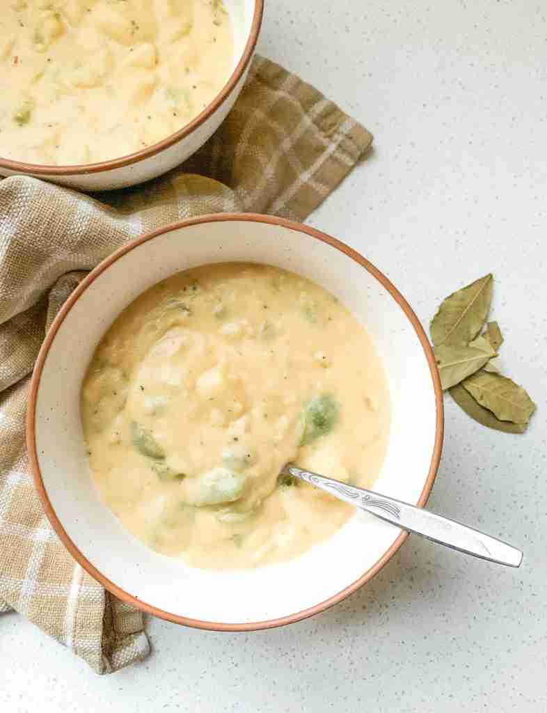 2 bowls of soup with bell peppers inside and bay leaves sitting by the bowl
