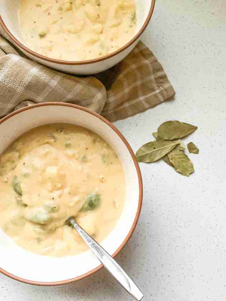 bowls of soup with veggies inside sitting on a towel with bay leaves beside it