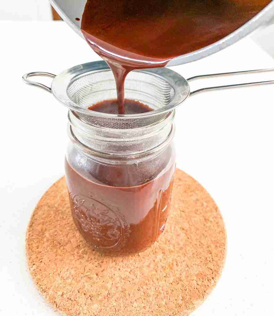 chocolate being poured out of a pan into a jar covered with a strainer