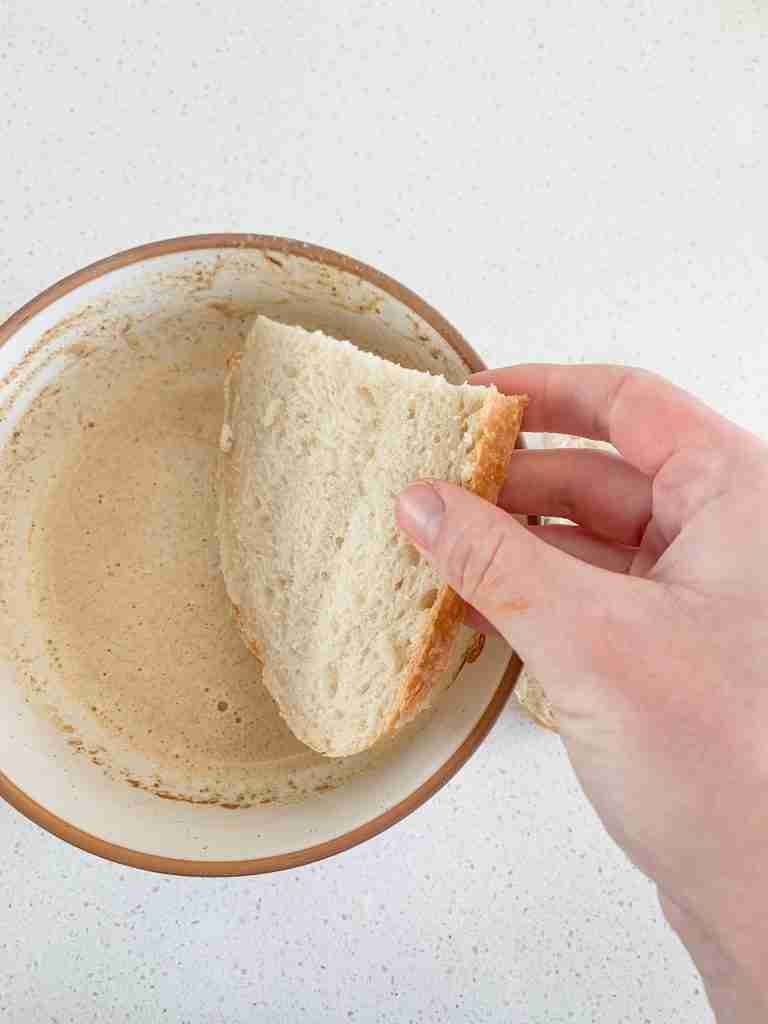 hand dipping bread slice into custard mix