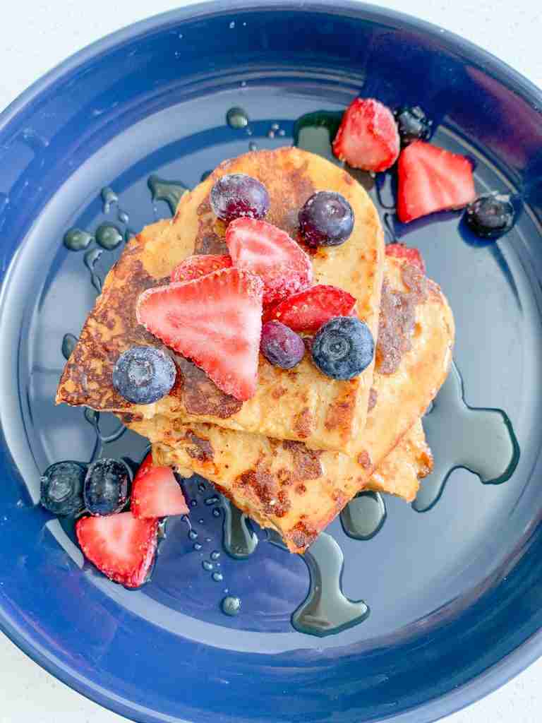 toast piled up on a plate with maple syrup drizzled over and berries on top 