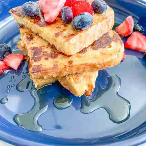 stack of toast with berries on top and maple syrup drizzled