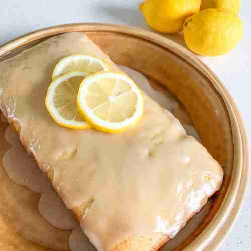 lemon cake on a plate with slices of lemons on top and lemons beside