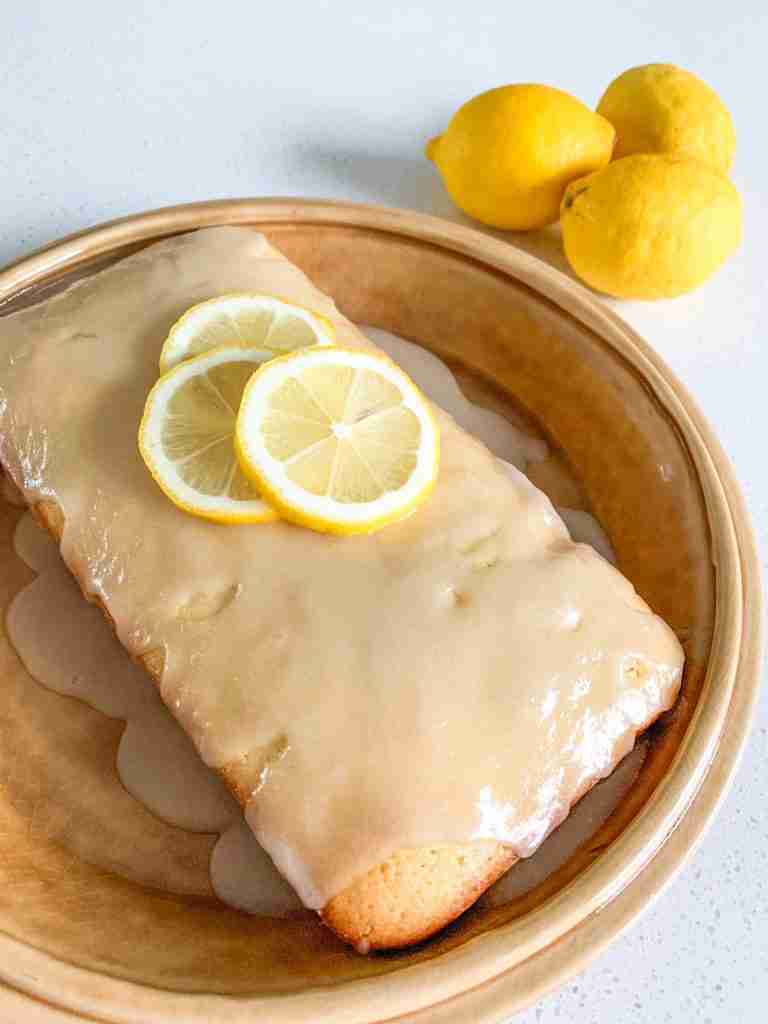 lemon cake on a plate with slices of lemons on top and lemons beside