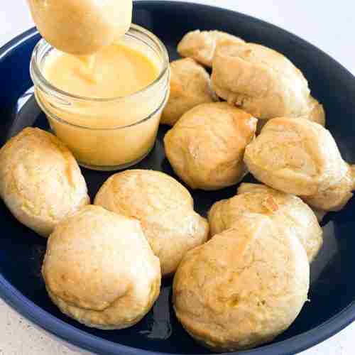 pretzels bites in a dish and one getting dipped into cheese by a hand