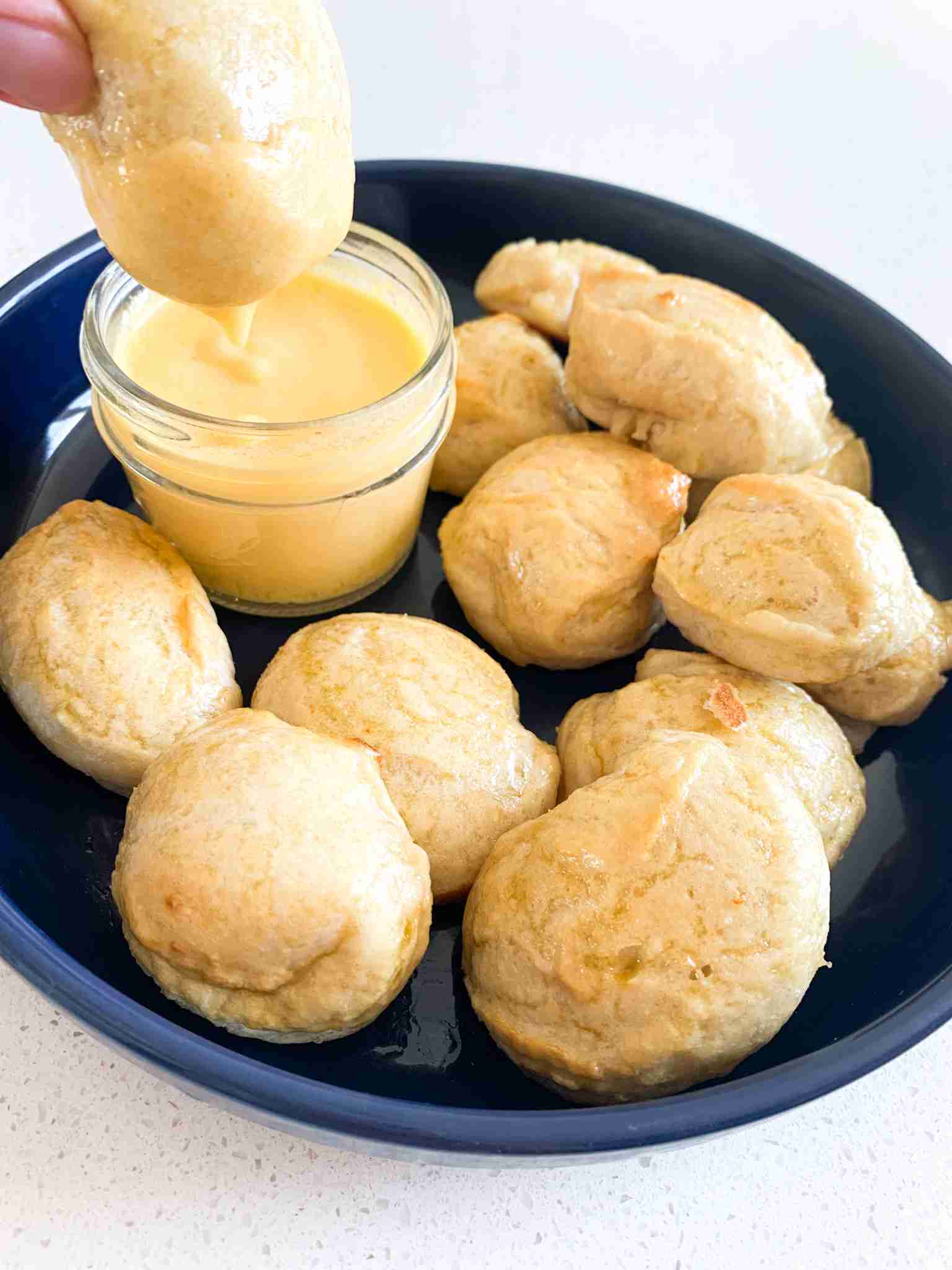 pretzels bites in a dish and one getting dipped into cheese by a hand