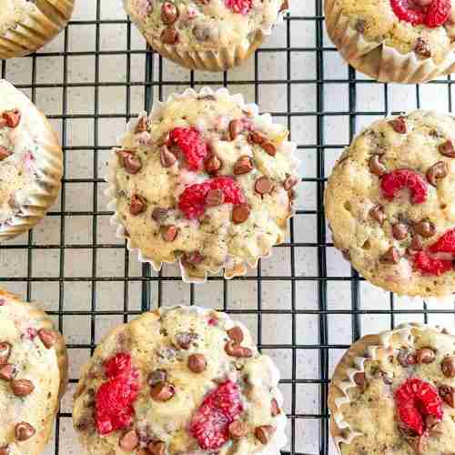 muffins on a cooling rack with raspberries and chocolate chips on top of them
