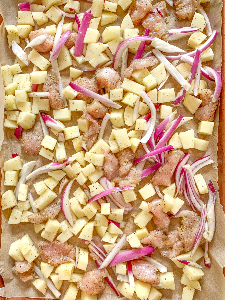 lemon chicken and potatoes spread out on sheet pan ready for baking