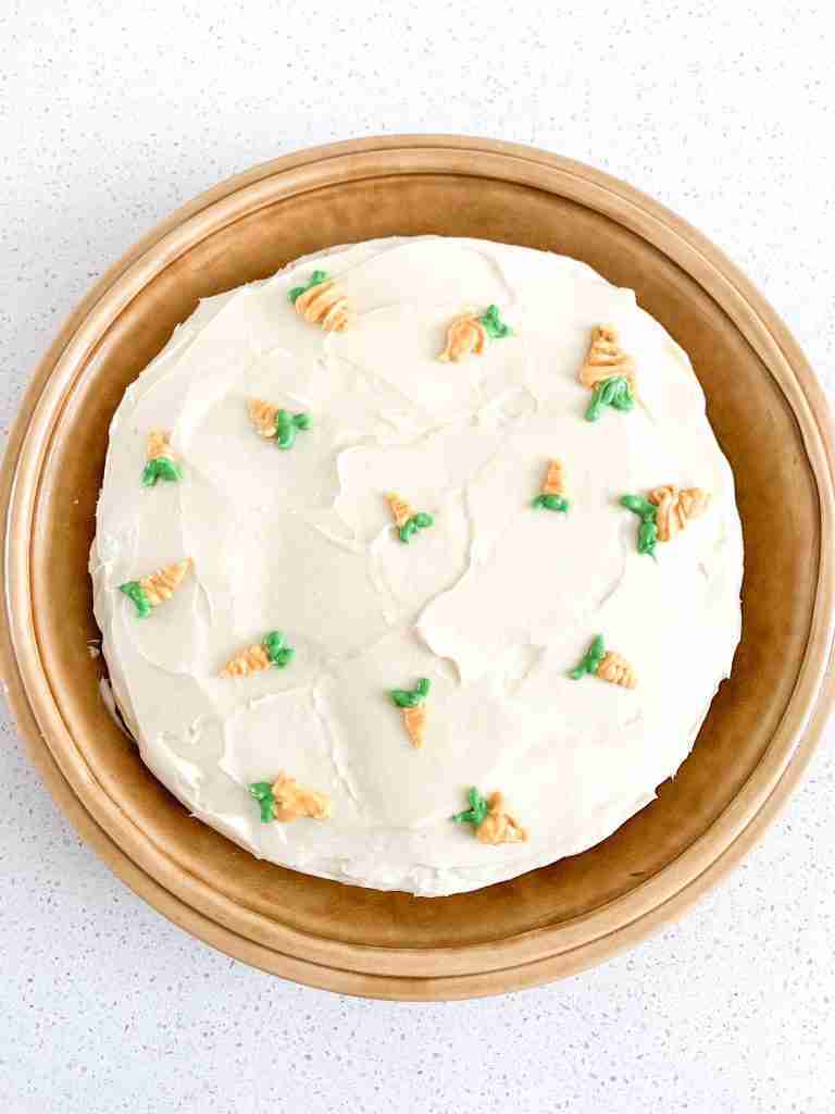 frosted cake sitting on a pie platter with carrots pipped on top