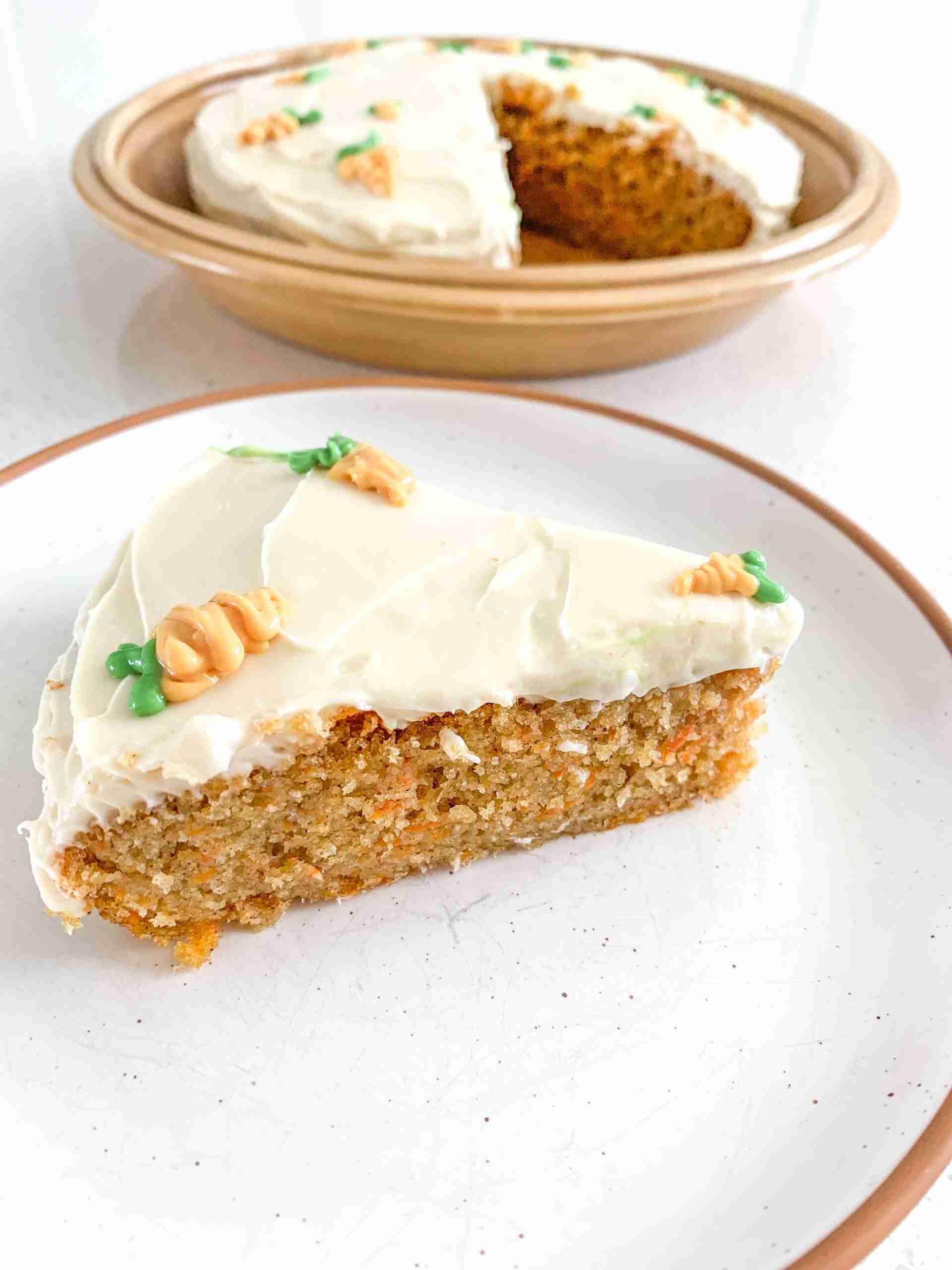 slice of cake on a plate in front of the full cake with little carrot decorations on top