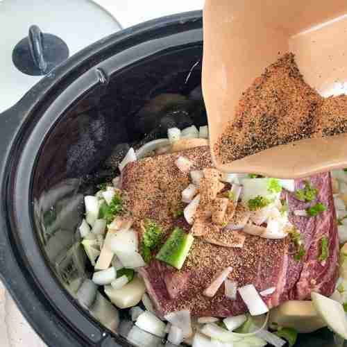 roast and veggies in a crock pot with seasoning being poured over