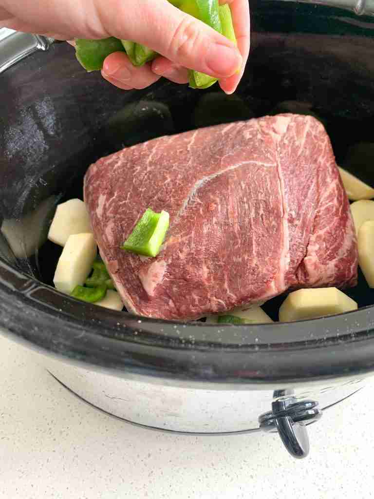 hand placing veggies around roast in a crockpot