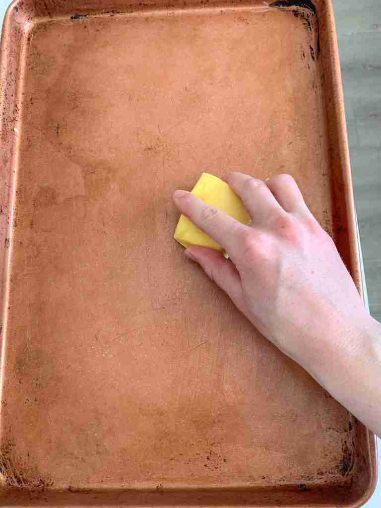 hand greasing a baking sheet with butter