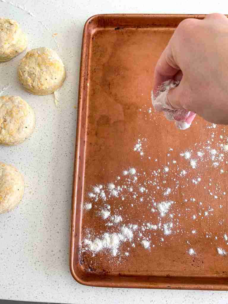 hand sprinkling flour on a baking sheet