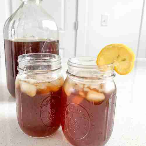2 glasses of tea, one with a lemon, and a jug of it behind
