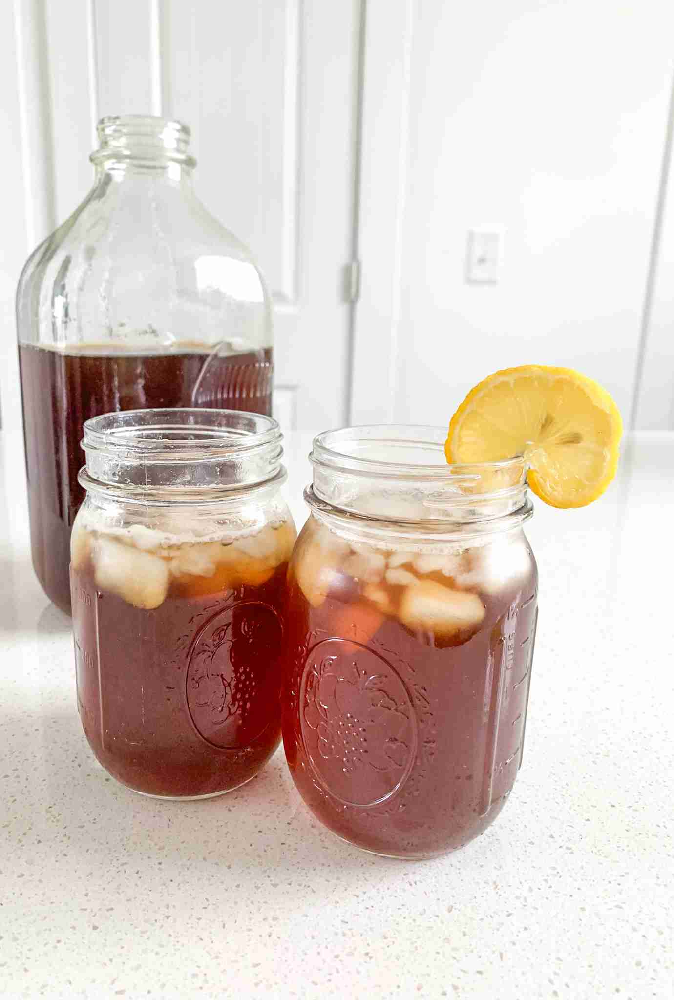 2 glasses of tea, one with a lemon, and a jug of it behind