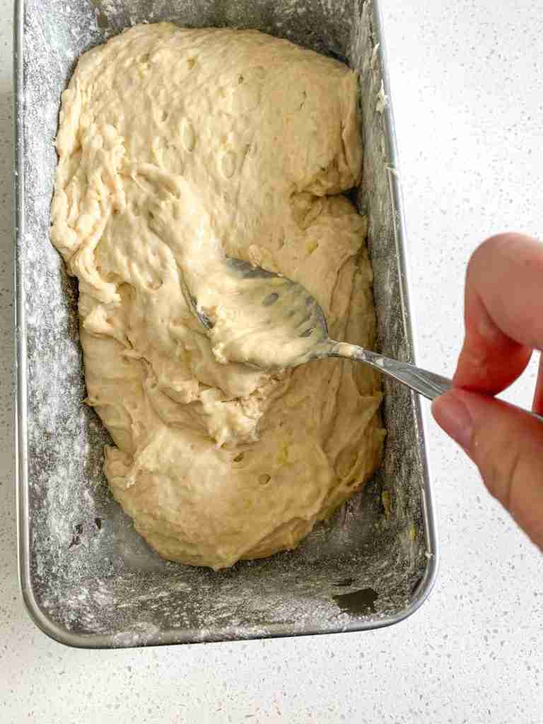 batter being smeared out in a loaf pan by hand