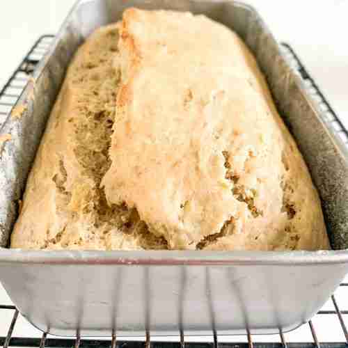 loaf of bread in a pan on a wire rack cooling