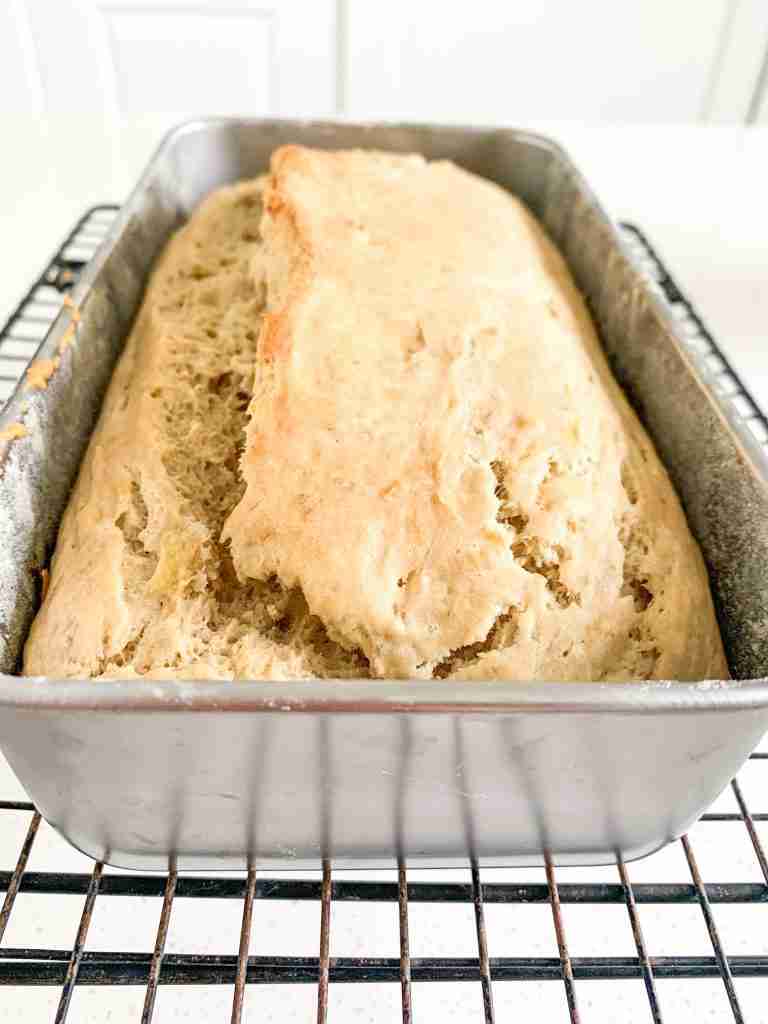 loaf of bread in a pan on a wire rack cooling
