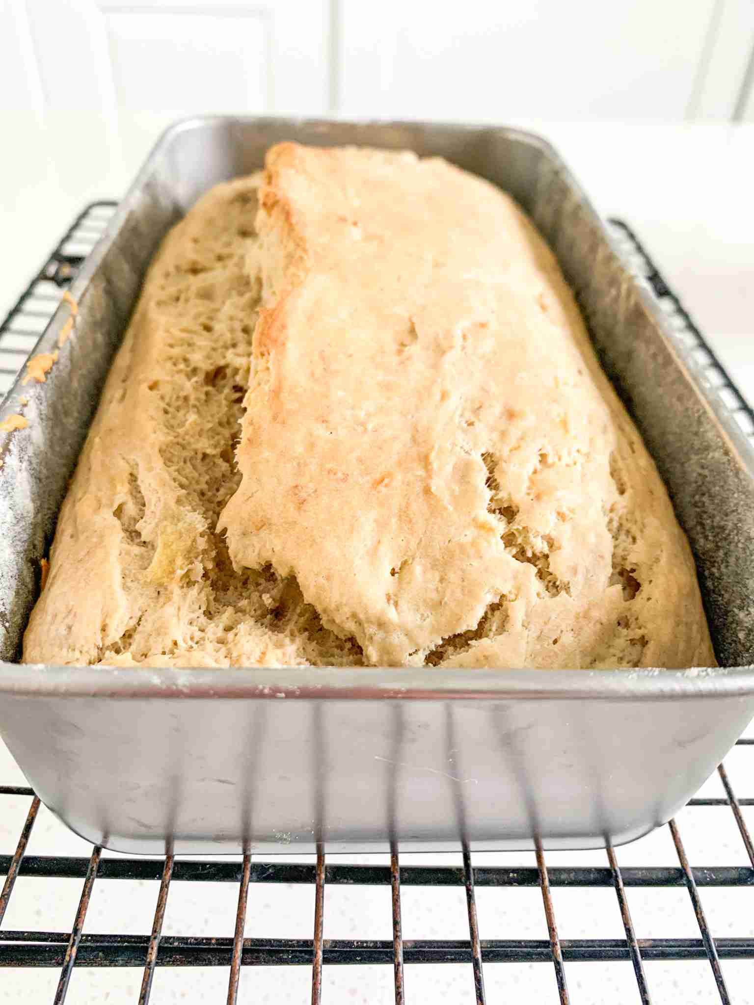 loaf of bread in a pan on a wire rack cooling