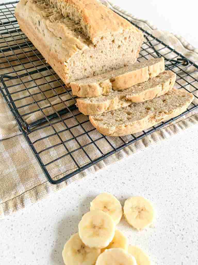 loaf of bread on a wire rack cooling with banana slices in front of it