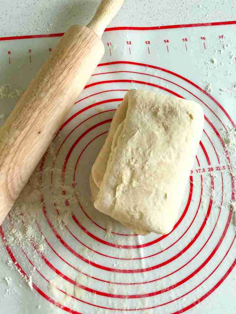 folded dough placed on a mat with rolling pin