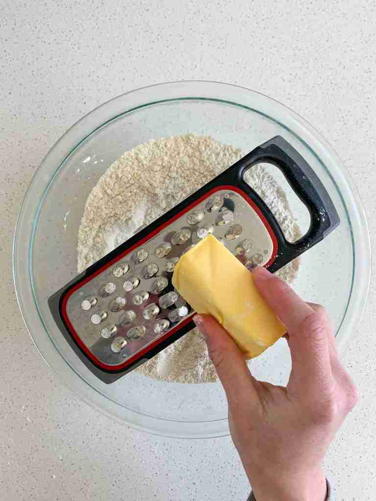 hand grating butter into flour over a bowl